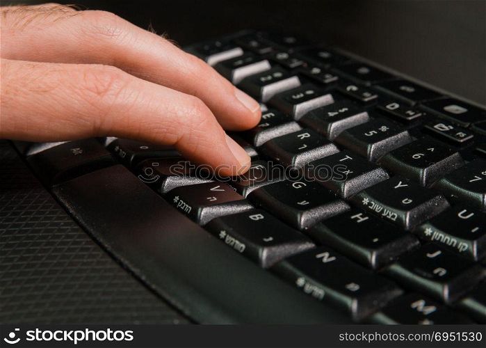 Man typing on a keyboard with letters in Hebrew and English - Wireless keyboard