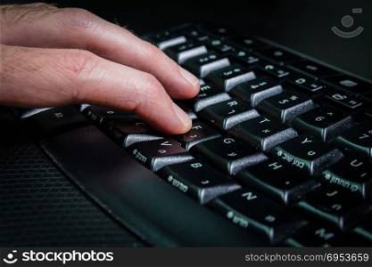 Man typing on a keyboard with letters in Hebrew and English - Wireless keyboard - Dark atmosphere