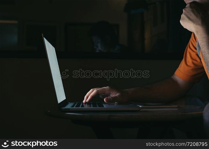 Man typing on keyboard and working at computer laptop in night.