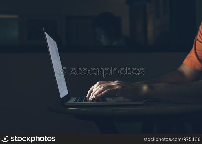 Man typing on keyboard and working at computer laptop in night.