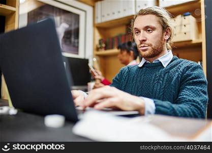Man typing on laptop at desk in traditional workshop