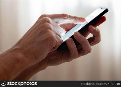 Man typing with the finger on the touch screen of a black smartphone close to the window with closed curtains at morning