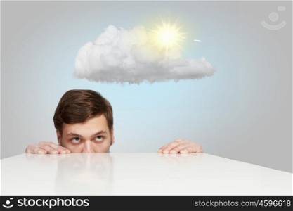 Man under table. Young businessman looking from under table at sun behind cloud