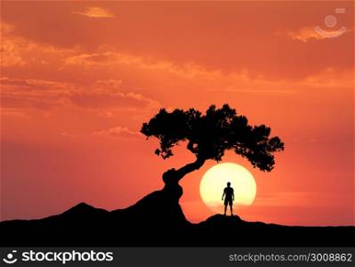 Man under the crooked tree on the background of sun. Silhouette of a standing sporty man on the mountain and colorful orange sky with clouds at sunset. Beautiful landscape in the evening. Travel