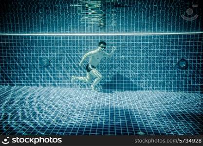 Man under water runs along the bottom of a swimming pool