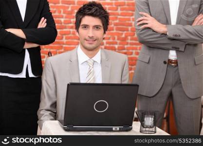 Man using a laptop flanked by people in suits