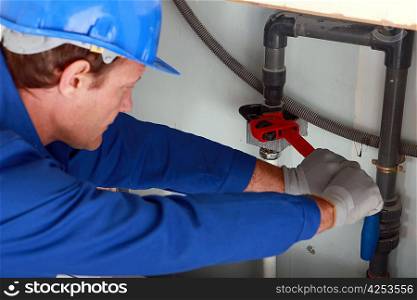 Man using a large red wrench on some interior water pipes