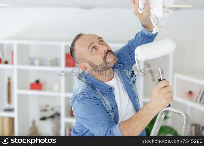 man using a paint roller on the ceiling