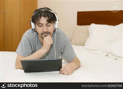 man using a tablet computer while lying in the bedroom