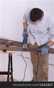 Man using an electric jigsaw to cut a piece of wooden flooring