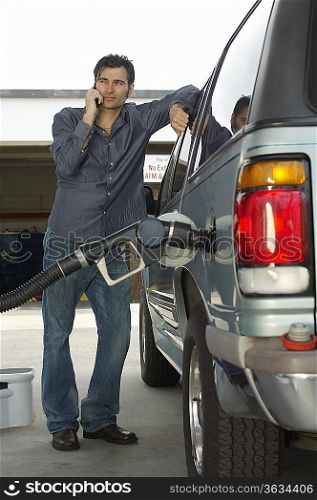 Man using cell phone leaning on van with fuel pump
