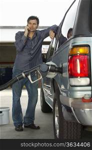Man using cell phone leaning on van with fuel pump