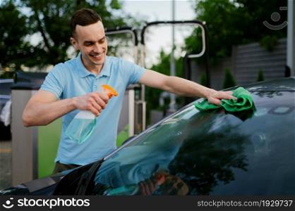 Man using cleaner and a rag, hand auto wash station. Car-wash industry or business. Male person cleans his vehicle from dirt outdoors. Man using window cleaner and a rag, hand auto wash