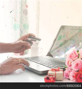 Man using computer and credit card with gift and roses on table, Shopping online. Valentines Day