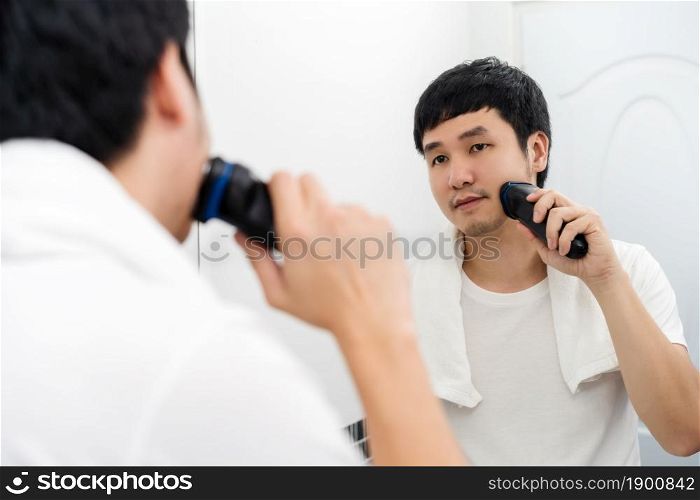 man using electric shave to shaving his face in the bathroom mirror