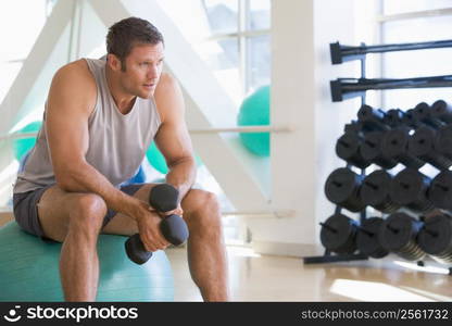 Man Using Hand Weights On Swiss Ball At Gym