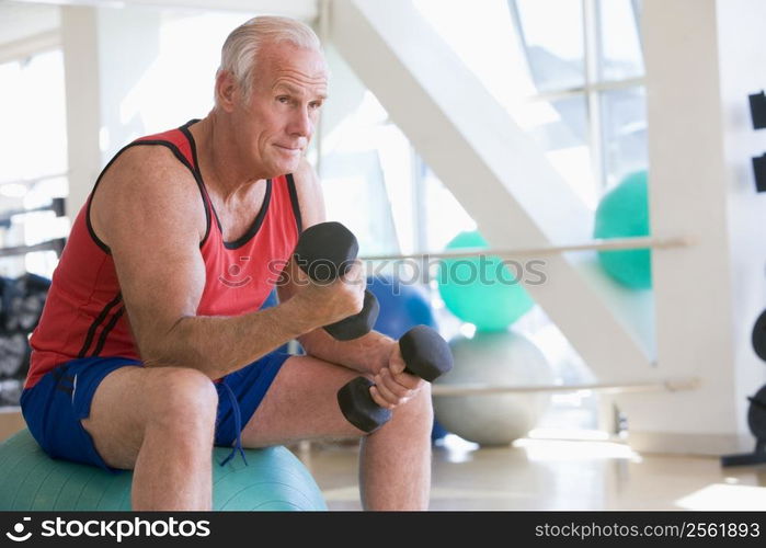 Man Using Hand Weights On Swiss Ball At Gym