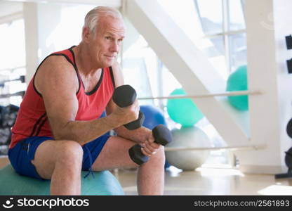 Man Using Hand Weights On Swiss Ball At Gym