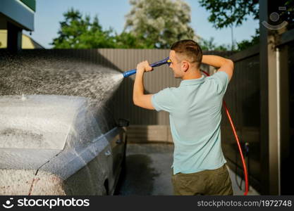 Man using high pressure water gun with foam, hand car wash station. Car-wash industry or business. Male person cleans his vehicle from dirt outdoors. Man using water gun with foam, hand car wash