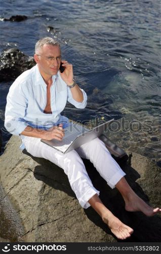 Man using his laptop by the water&rsquo;s edge