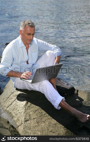 Man using his laptop by the water&rsquo;s edge