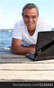Man using his laptop on a wooden jetty