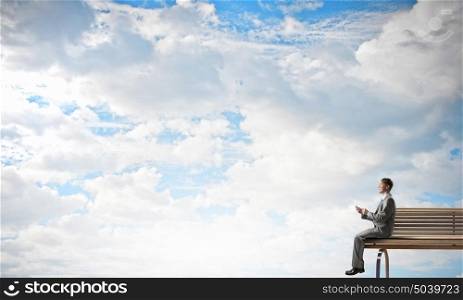 Man using his mobile phone. Young businessman sitting on bench with mobile phone in hand
