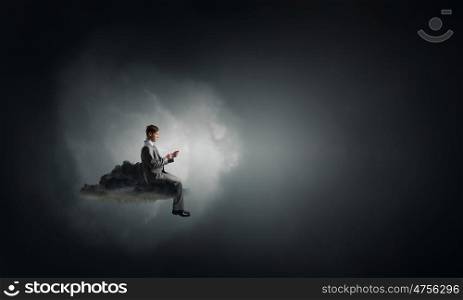 Man using his mobile phone. Young businessman sitting on black cloud with mobile phone in hands
