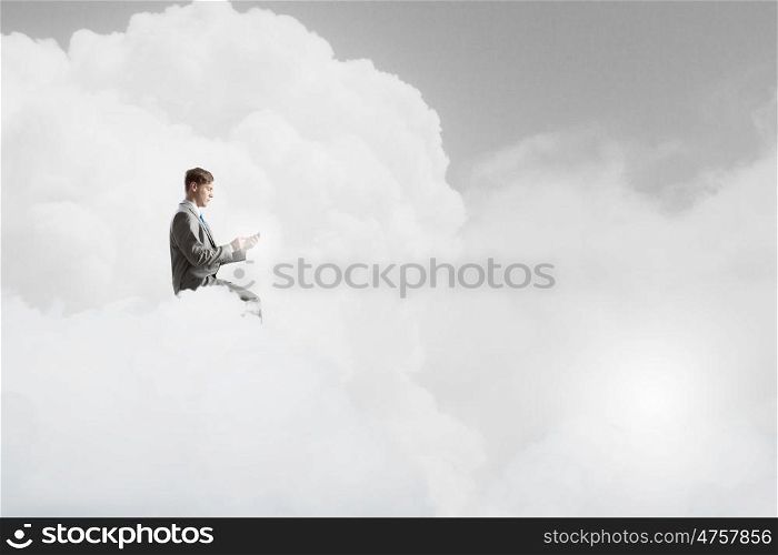 Man using his mobile phone. Young businessman sitting on cloud with mobile phone in hands