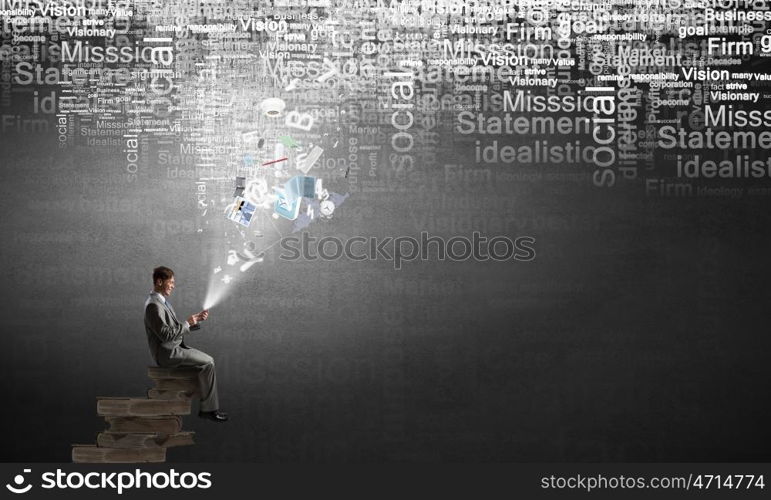 Man using his mobile phone. Young businessman sitting on pile of books with mobile phone in hand