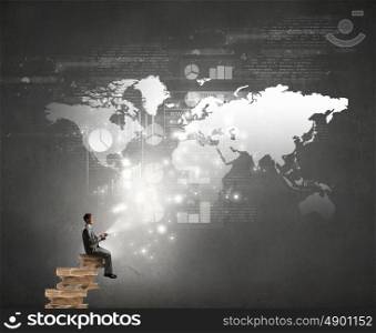 Man using his mobile phone. Young businessman sitting on pile of books with mobile phone in hand
