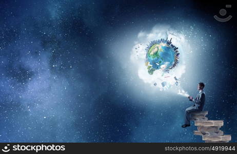 Man using his mobile phone. Young businessman sitting on pile of books with mobile phone in hand. Elements of this image are furnished by NASA