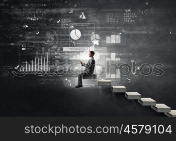 Man using his mobile phone. Young businessman sitting on steps with mobile phone in hand