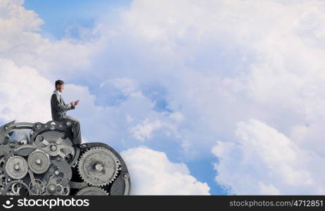 Man using his smartphone application. Young businessman sitting on gears mechanism with mobile phone in hand