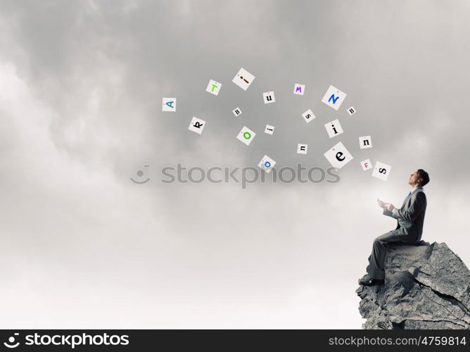 Man using his smartphone application. Young businessman sitting on top of rock with mobile phone in hand