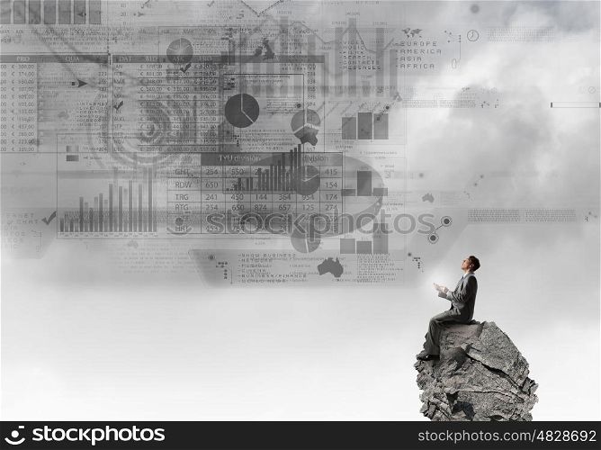 Man using his smartphone application. Young businessman sitting on top of rock with mobile phone in hand