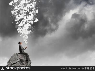 Man using his smartphone application. Young businessman sitting on top of rock with mobile phone in hand