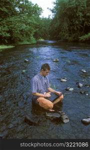 Man Using Laptop Computer In The Middle Of A Mountain Stream