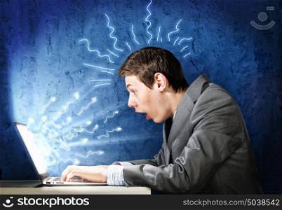 Man using laptop. Young businessman looking shocked into laptop monitor