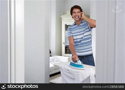 Man using mobile phone and ironing in living room
