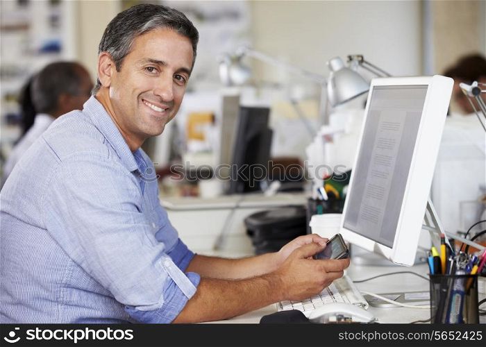 Man Using Mobile Phone At Desk In Busy Creative Office