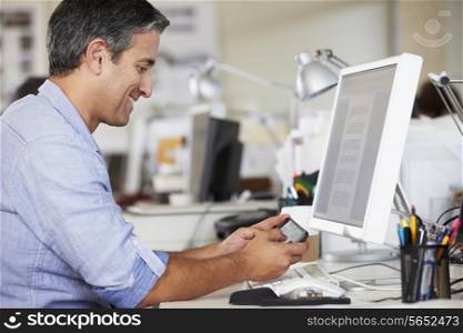 Man Using Mobile Phone At Desk In Busy Creative Office