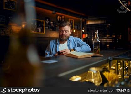 Man using mobile phone at the counter in bar. One male person resting in pub, human emotions, leisure activity, nightlife. Man using mobile phone at the counter in bar