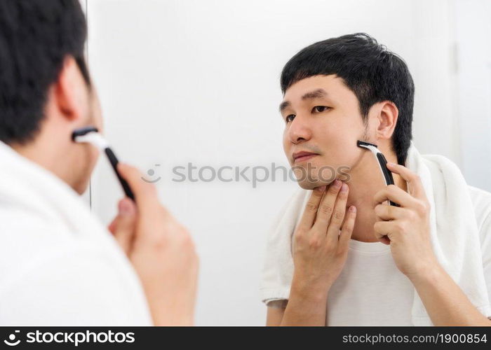 man using razor to shaving his face without foam, dry shave in the bathroom mirror