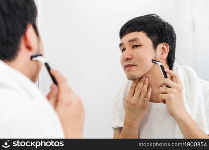 man using razor to shaving his face without foam, dry shave in the bathroom mirror