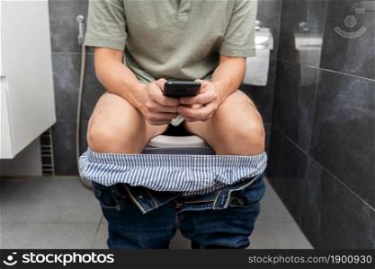 man using smartphone and sitting in toilet bowl in the bathroom at home