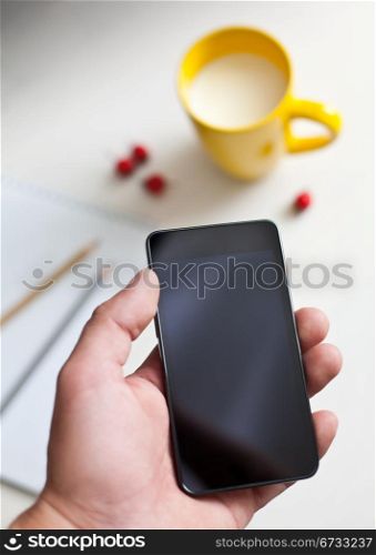 Man using smartphone, close-up, cup of milk and planning book on the background