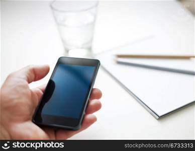 Man using smartphone, cup of water and notebook on the background