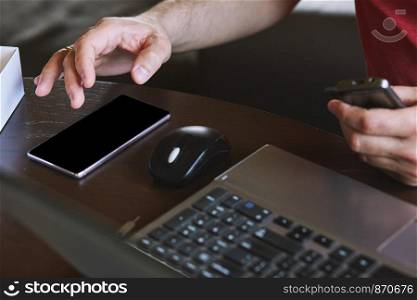 Man using smartphone working on laptop sitting at a desk