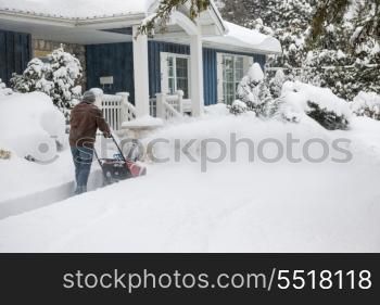 Man using snowblower in deep snow. Man using snowblower to clear deep snow on driveway near residential house after heavy snowfall